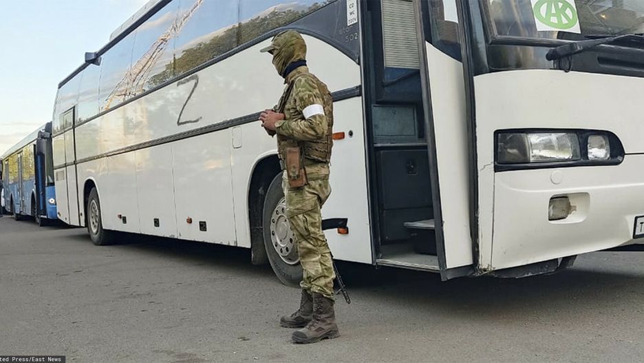 Rosyjski żołnierz pilnuje autobusu z ukraińskimi żołnierzami