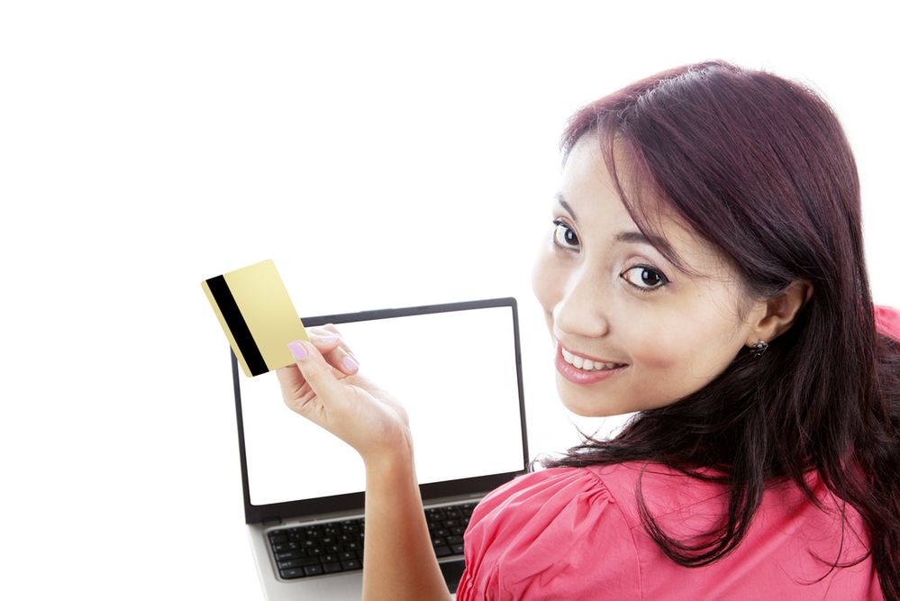 Zdjęcie Smiling young woman holding credit card for online shopping with laptop isolated on white pochodzi z serwisu Shutterstock