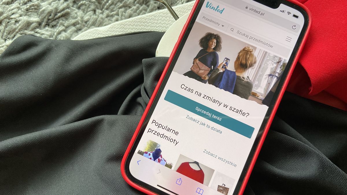 Na zdjęciu strona Vinted.pl włączona na telefonie, który leży na ciuchach