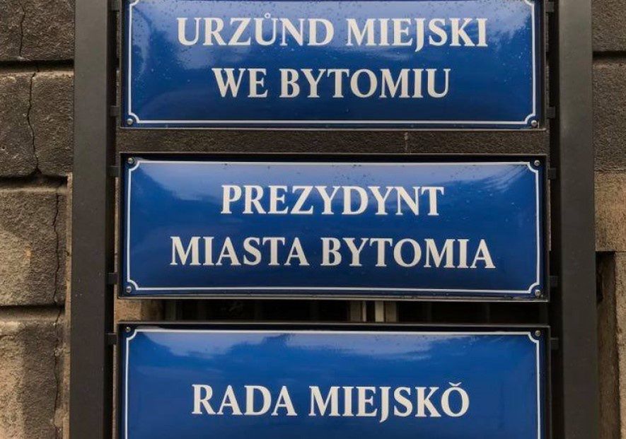 Śląskie. Na budynku Urzędu Miejskiego w Bytomiu zawisły flagi województwa śląskiego, a przed wejściem do budynku tabliczki urzędowe po śląsku.