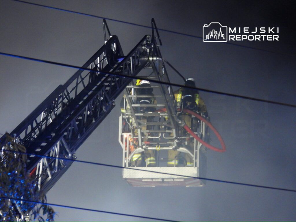 Strażacy w podnośniku gaśniczym prowadzą akcję ratunkową w gęstej mgle.