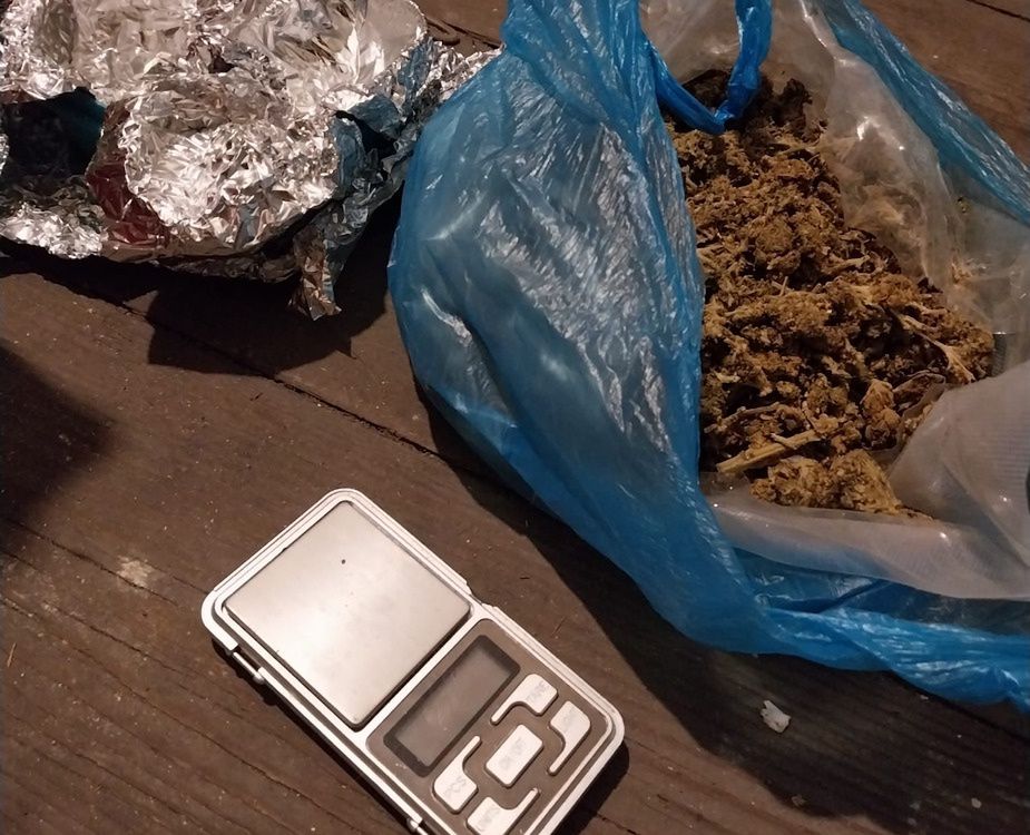 Pakunek z suszem roślinnym w niebieskiej torbie obok folii aluminiowej i wagi elektronicznej na drewnianej podłodze.