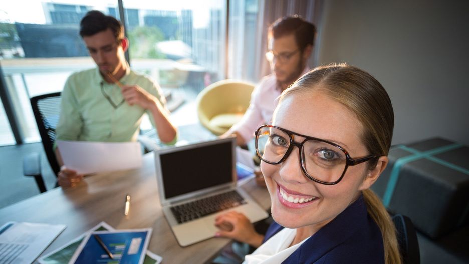 Businesswoman smiling at camera while her colleagues reading document in the background