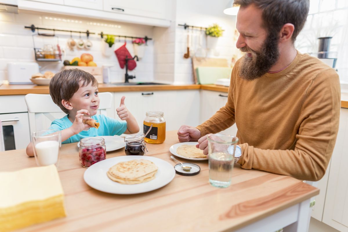 Lovely young boy eating homemade pancakes with honey