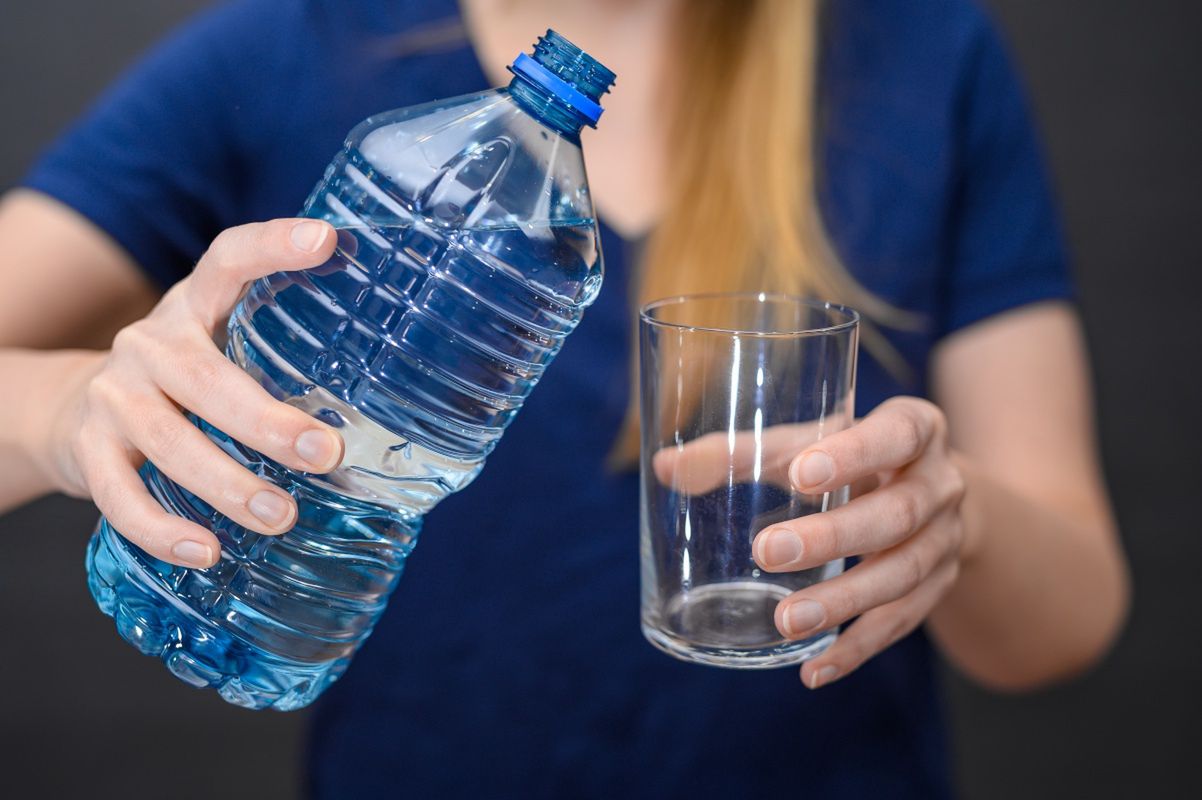 A woman pouring water into a glass from a plastic bottle