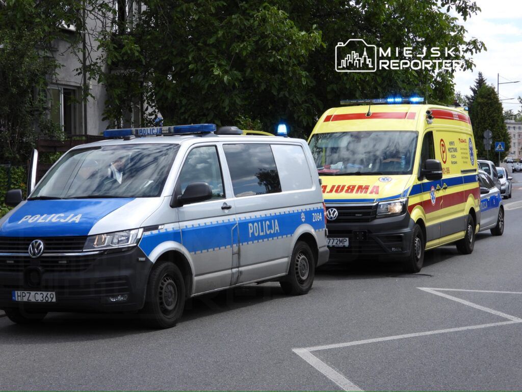 Policyjny pojazd oraz ambulans z włączonymi sygnałami świetlnymi zatrzymane na ulicy w miejskim otoczeniu.