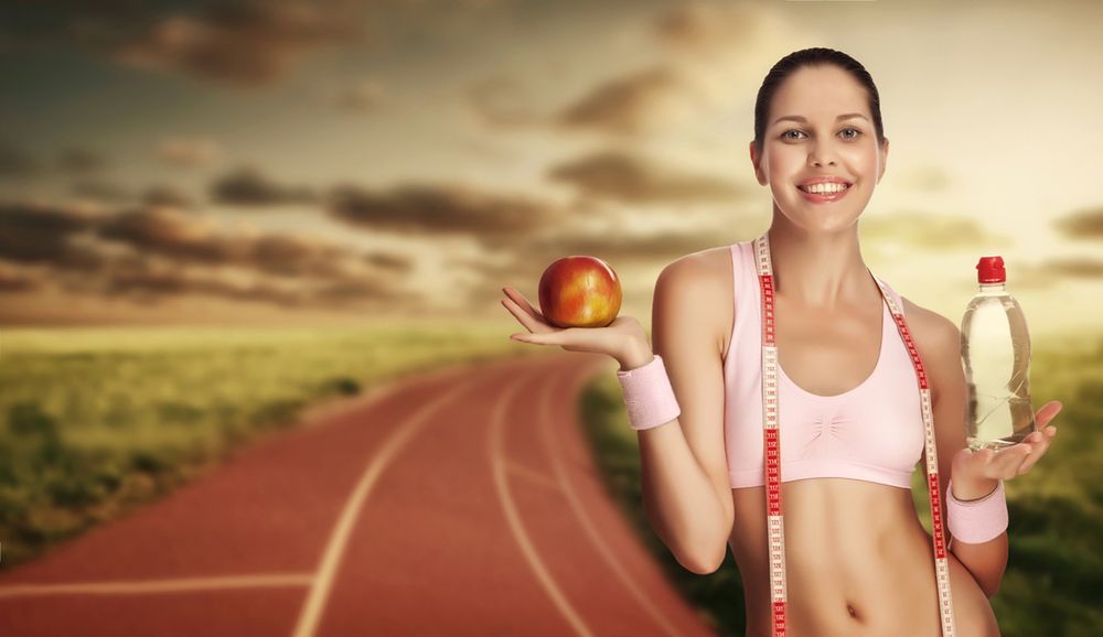 A young athletic woman holding water and apple against running track