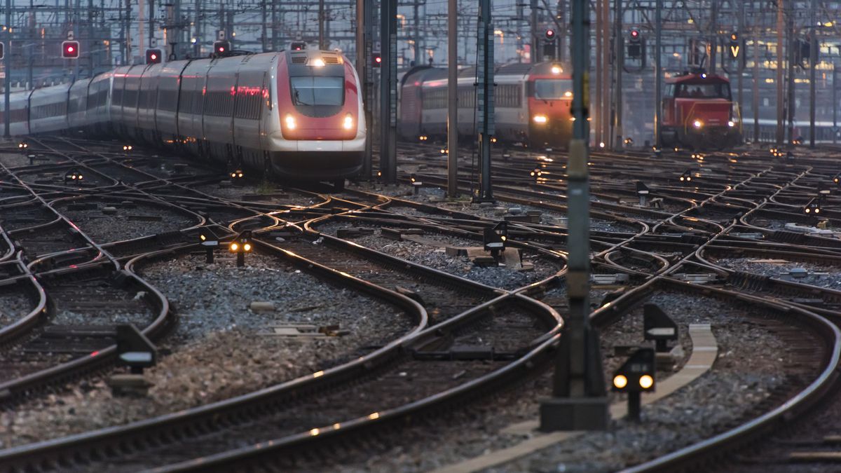 Commuter train approaching busy railway track field at twilightIn the early morning twilight, several commuter trains are approaching a busy railway station.EThamPhotocatenary, points