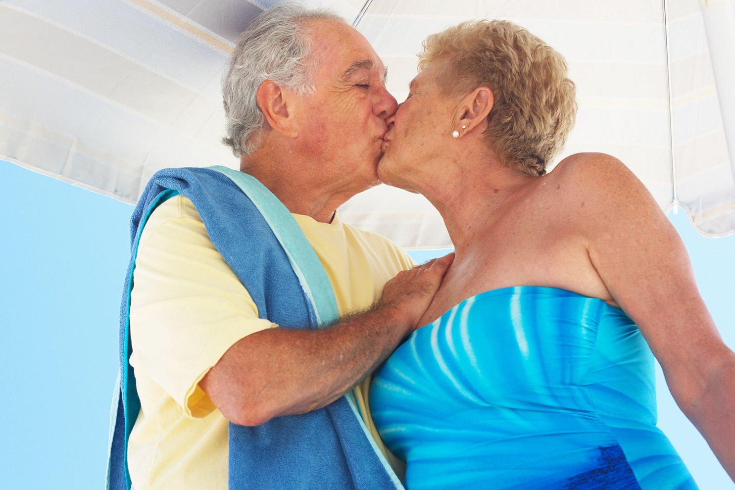 Senior couple kissing under beach umbrella, three quarter lengthChristopher RobbinsEasy Retouch, Colour, Photography, horizontal, outdoors, day, low angle view, three quarter length, embracing, standing, casual clothing, senior adult, 70-75 years, senior women, senior men, adults only, husband, wife, two people, couple, young at heart, retirement, active seniors, beach, one piece swimsuit, romance, affection, love, Caucasian, kissing, beach, umbrella, towel
