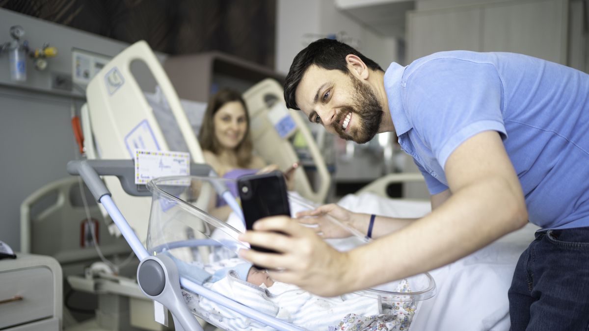 Happy father taking a selfie of his newborn and wife in the hospital