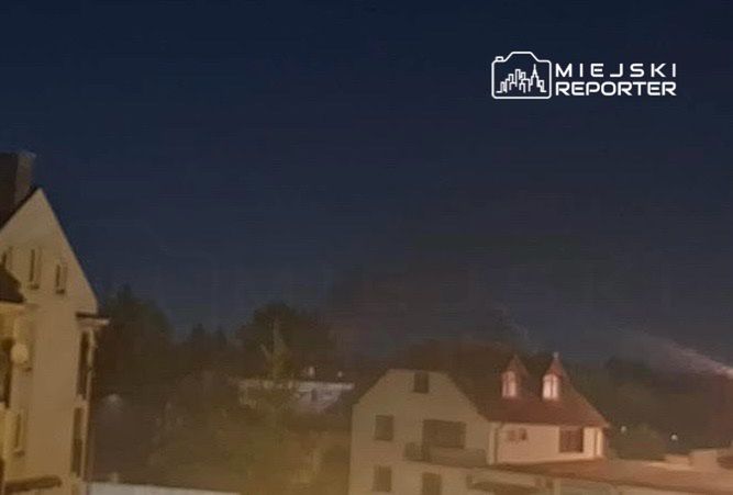 Nocny widok na miasto z oświetlonymi budynkami w tle oraz ciemnym niebem.