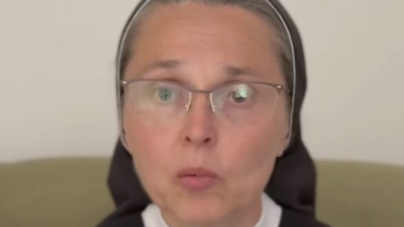 Kobieta w habicie zakonnym mówi do kamery, trzymając dłonie złożone na kolanach.