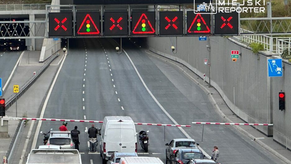 Zatrzymany ruch w tunelu, sygnalizacja świetlna w kolorze czerwonym, widoczne samochody czekające na wjazd.