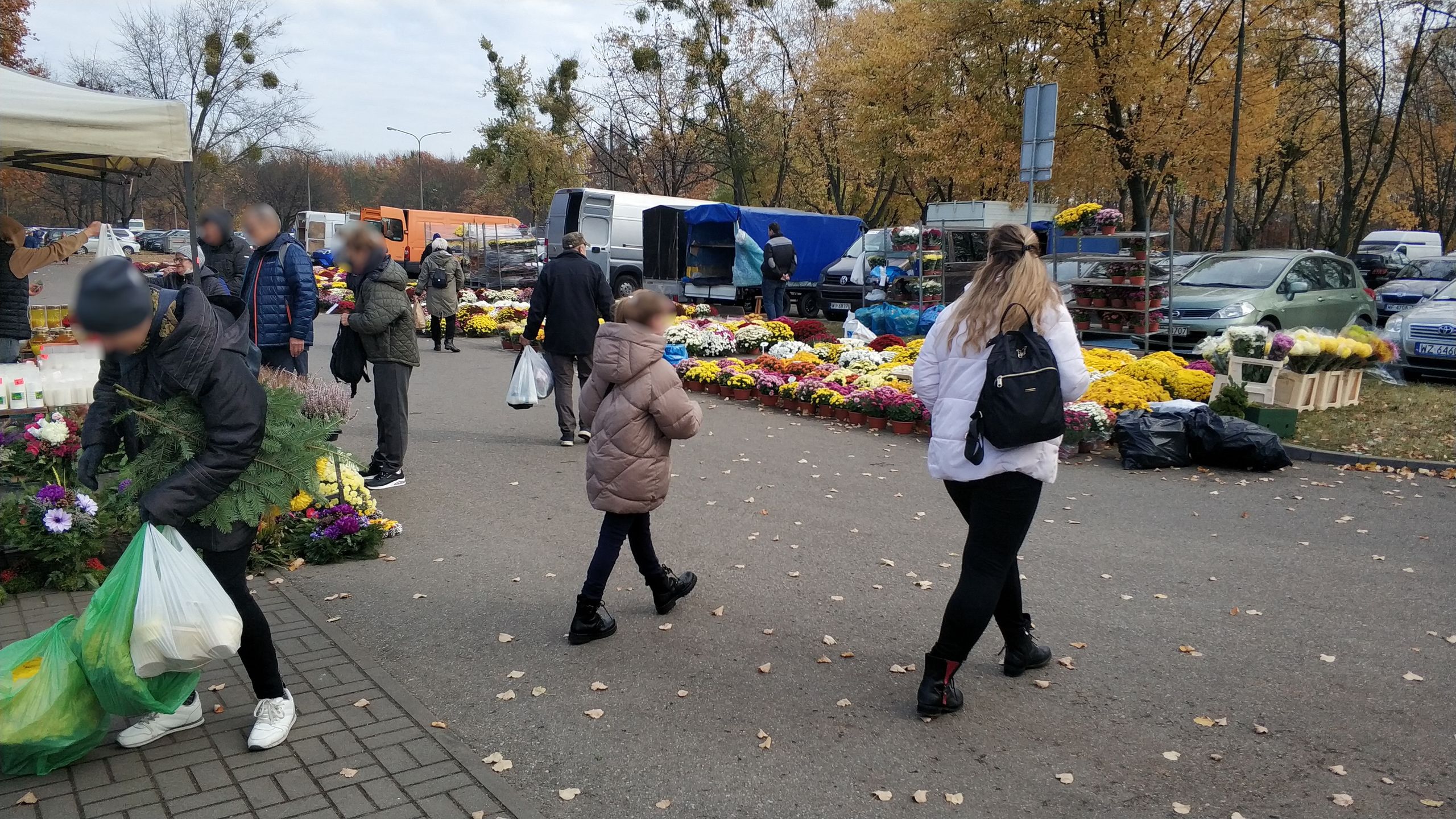 Zdjęcie przedstawia odwiedzających cmentarz i kupujących kwiaty