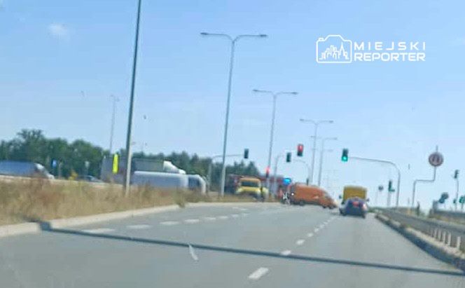 Ruch drogowy na skrzyżowaniu z sygnalizacją świetlną, widoczne ciężarówki i samochody osobowe.