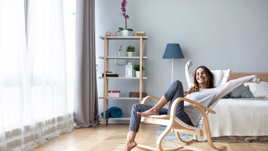 Happy woman resting comfortably sitting on modern chair in the living room at home. 