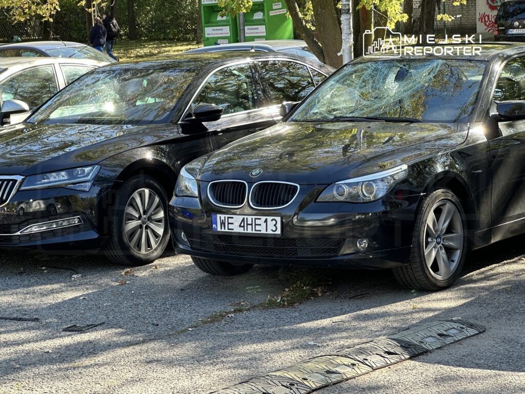 Dwa czarne samochody zaparkowane obok siebie na ulicy, w tle widać drzewa i przechodniów.