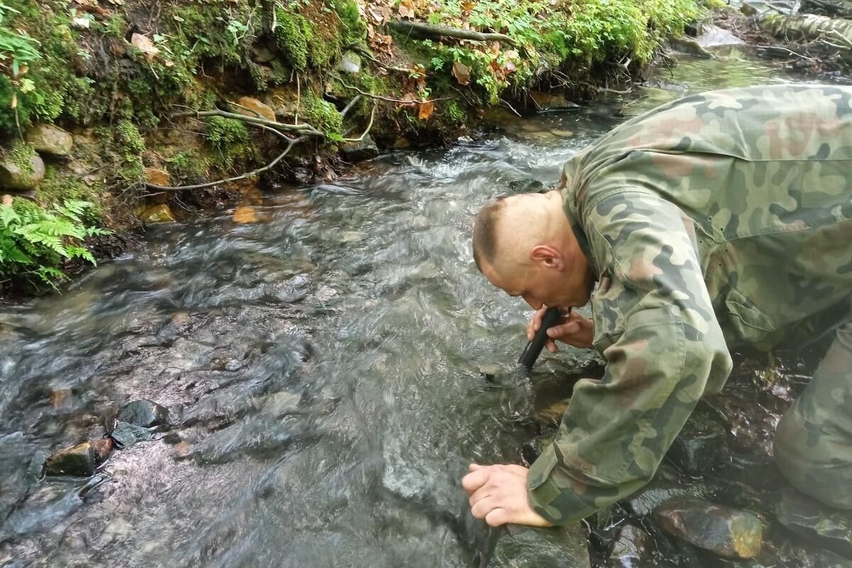 mężczyzna pije wodę ze strumyka