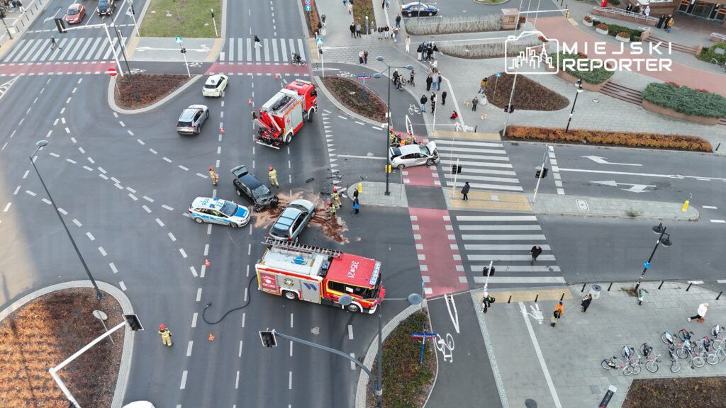 Wielki wypadek drogowy na skrzyżowaniu, gdzie straż pożarna i policja zabezpieczają miejsce zdarzenia.
