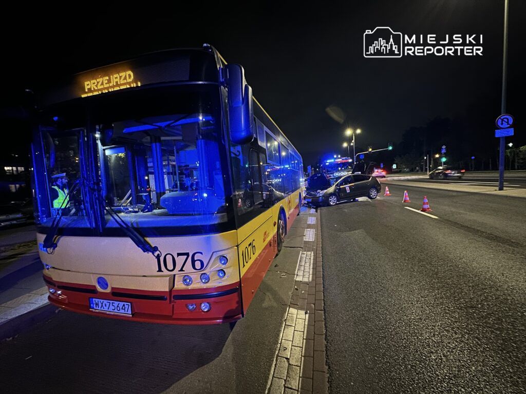 Autobus z numerem 1076 zatrzymany na drodze, obok uszkodzony samochód osobowy z otwartą maską i trójkąty ostrzegawcze.