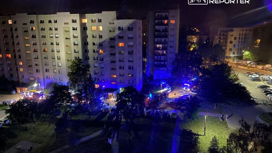 W nocy przed budynkiem mieszkalnym z niebieskimi i czerwonymi światłami interwencyjnymi zgromadziły się służby ratunkowe.