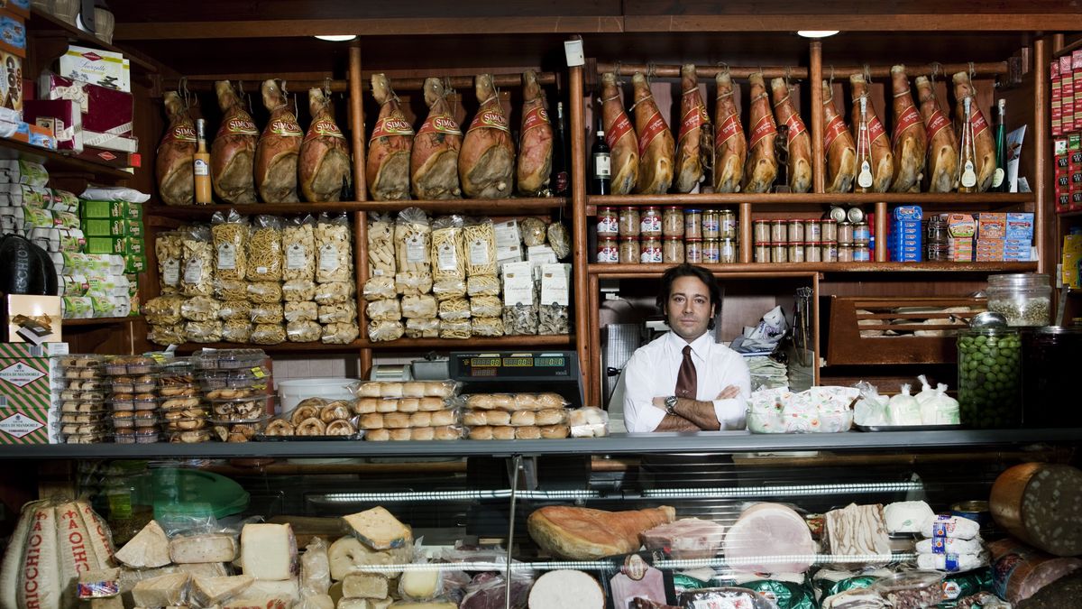 a grocer behind his counter in his shopA young grocer stands behind his counter. You see the beautiful arranged display of his crocery store. He offers cheese, ham, sausages, bread, pasta, olives and all the fancy food people loveFrank Rothefood, independent, business, fresh, biological