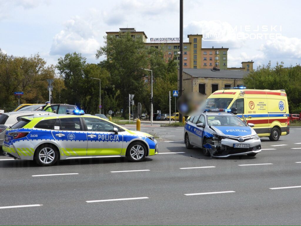 W miejscu zdarzenia widać uszkodzone radiowozy policyjne oraz ambulans, na drodze z widocznymi śladami kolizji.