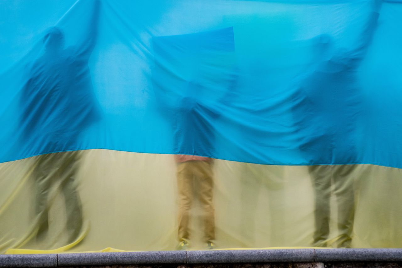 Sylwetki protestujących ludzi schowanych za wielką flagą Ukrainy podczas manifestacji w Madrycie. W wydarzeniu wzięło udział ponad 12 tys. ludzi.