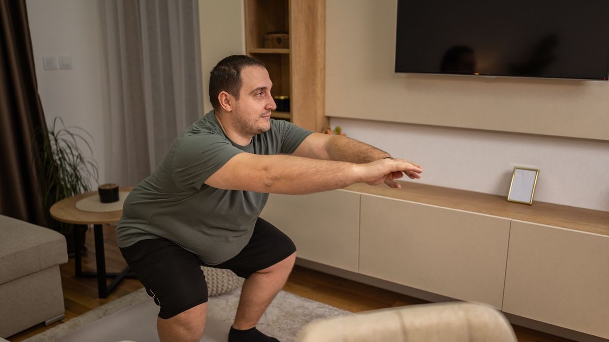 Overweight man doing squat exercise in living room
Overweight man doing squats for home workout to improve fitness and health
MSTORY