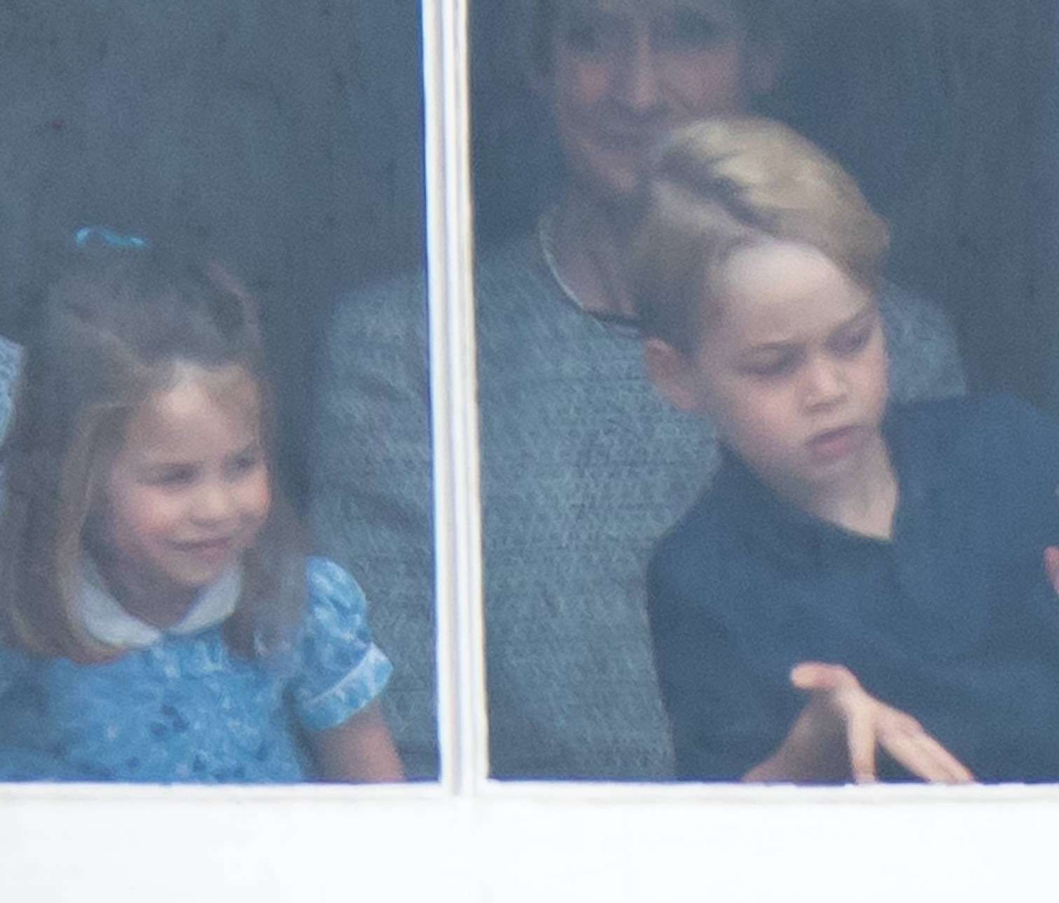 Księżniczka Charlotte i książę George stroją miny w oknie Pałacu Buckingham