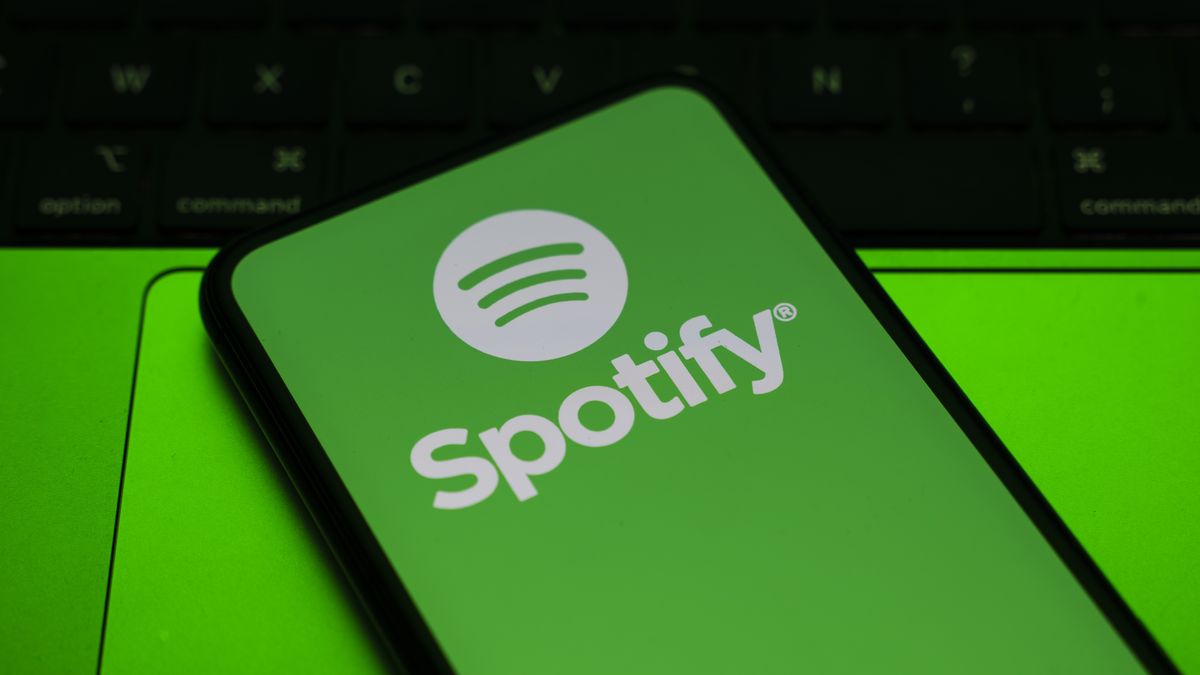 In Créteil, France, on September 29, 2025, the Spotify logo appears on a smartphone placed on a laptop keyboard, which reflects a green light. Spotify removes 75 million AI-generated tracks and now requires them to be labeled "AI generated." (Photo Illustration by Samuel Boivin/NurPhoto via Getty Images)
