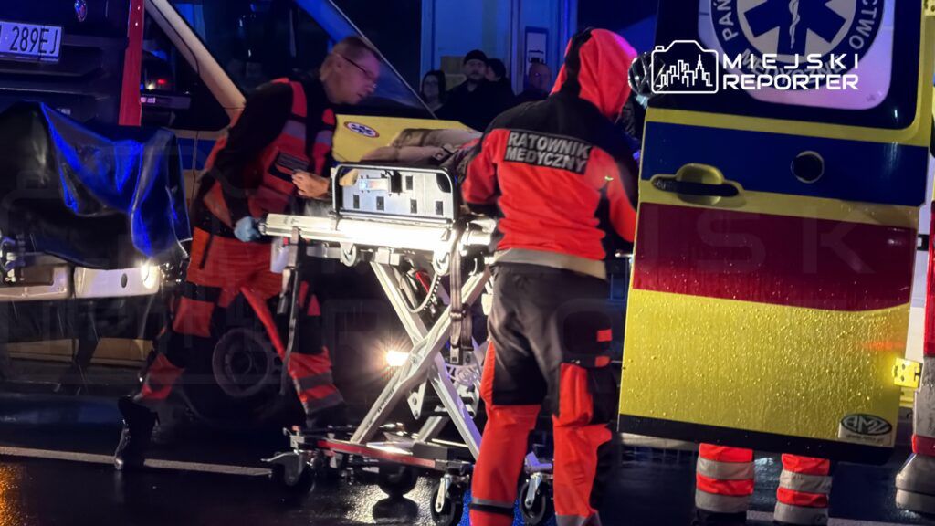Ratownicy medyczni transportują poszkodowanego na noszach w pobliżu karetki w nocy.