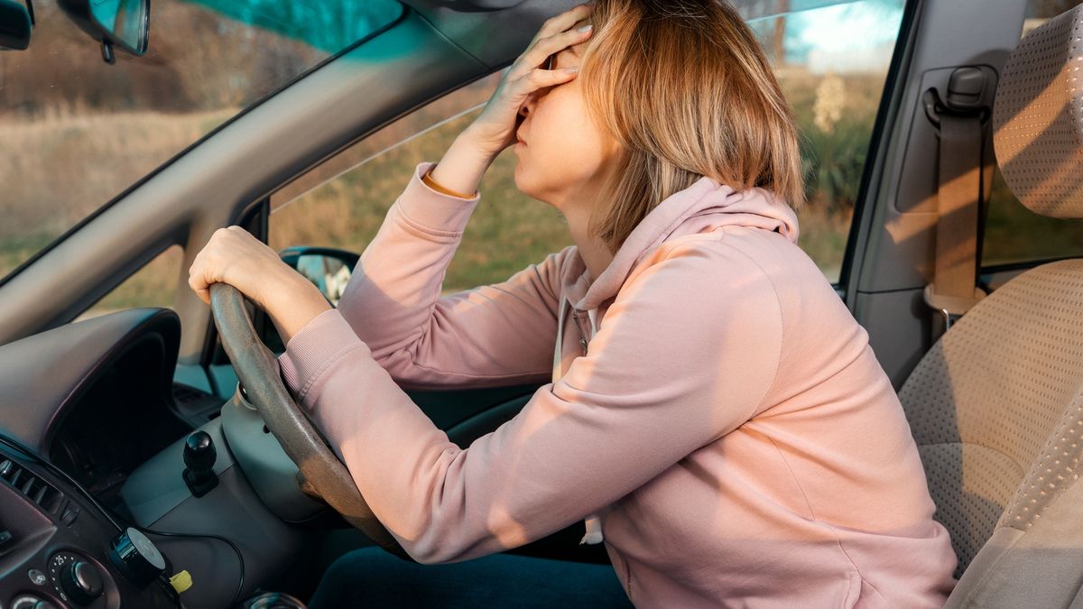 A stressed woman is sitting behind the wheel of a car and holding her head in despair.A young blonde sad woman is sitting behind the wheel of a car and holding her head in despair, covering her eyes with her hand. Side view. Stress while driving a right-hand drive car.Ildar Abulkhanov