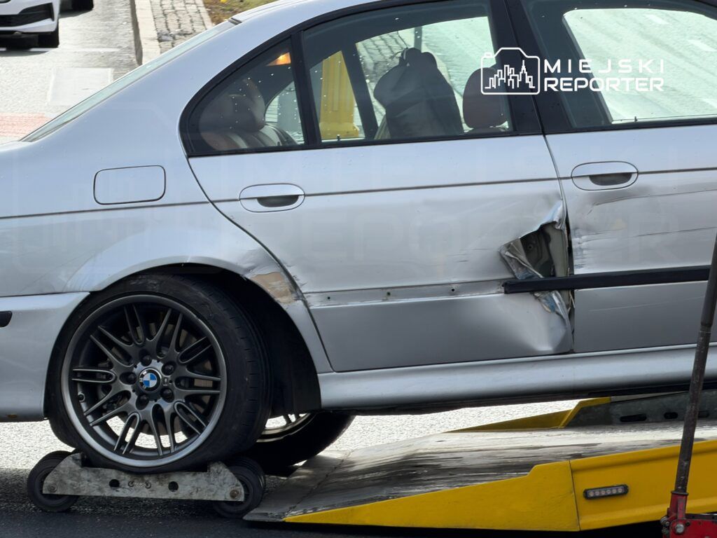 Uszkodzony samochód marki BMW z wgniecioną karoserią stoi na lawecie na ulicy.