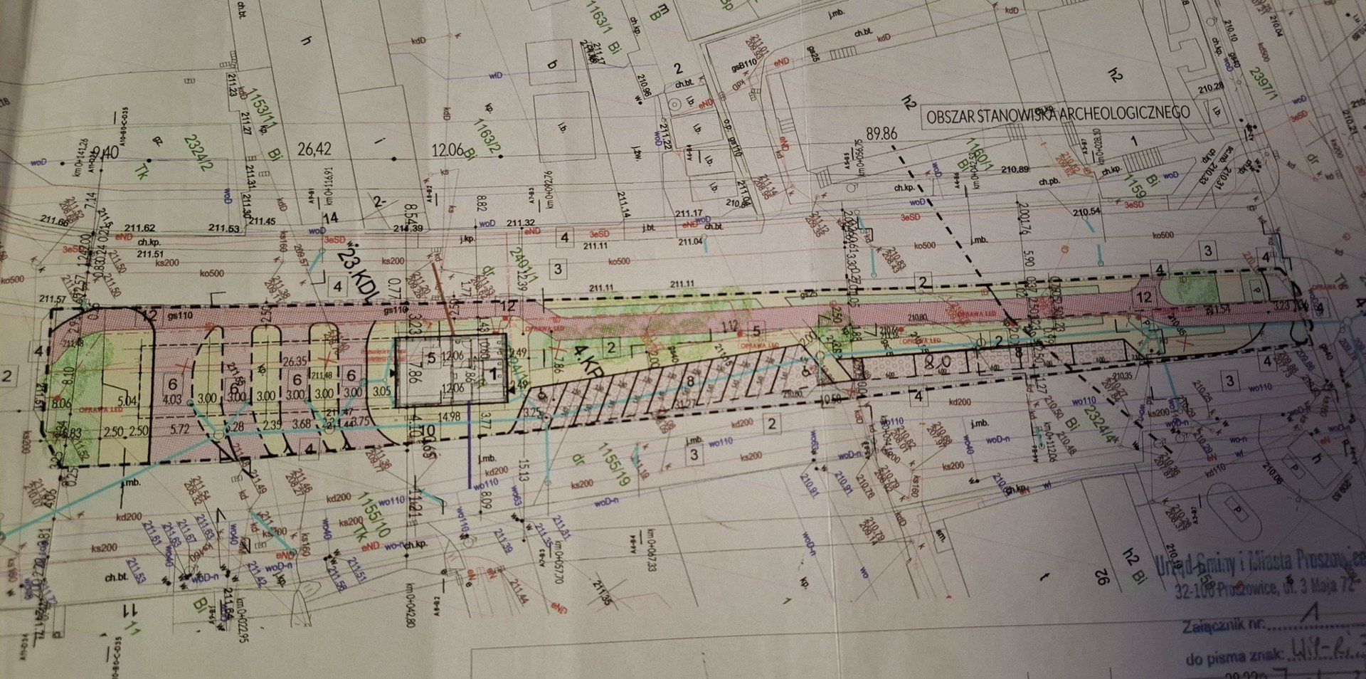 Ulica Kolejowa w Proszowicach, projekt przebudowy istniejącego parkingu. Na czerwono zaznaczona ścieżka rowerowa. Prostokąt w środku to przyszła poczekalnia. Z jego lewej strony zaznaczone perony autobusowe, z prawej miejsca postojowe dla samochodów.