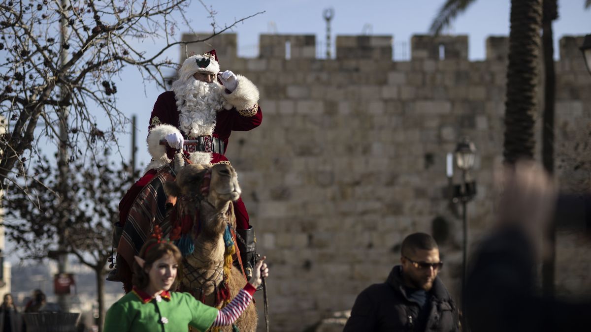 JERUSALEM - DECEMBER 22: A man dressed up as Santa Claus and a woman dressed up as an elf tour the city walls with a camel ahead of Christmas in Jerusalem on December 22, 2022. (Photo by Mostafa Alkharouf/Anadolu Agency via Getty Images)
