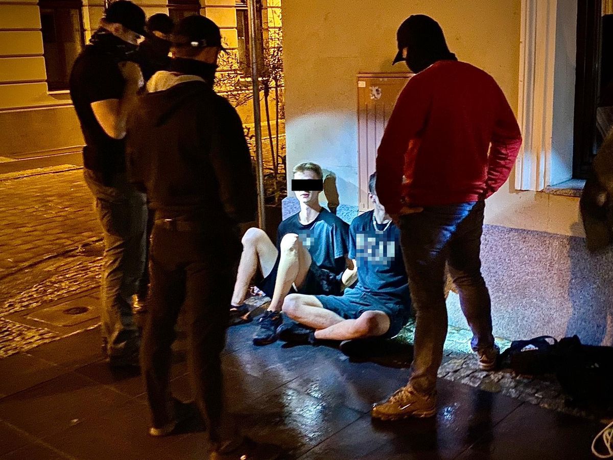 Zatrzymani dwaj mężczyźni w nocy siedzą na płycie starego rynku. Przy nich w półokręgu stoją policjanci po cywilnemu.(Fot: KWP Bydgoszcz)