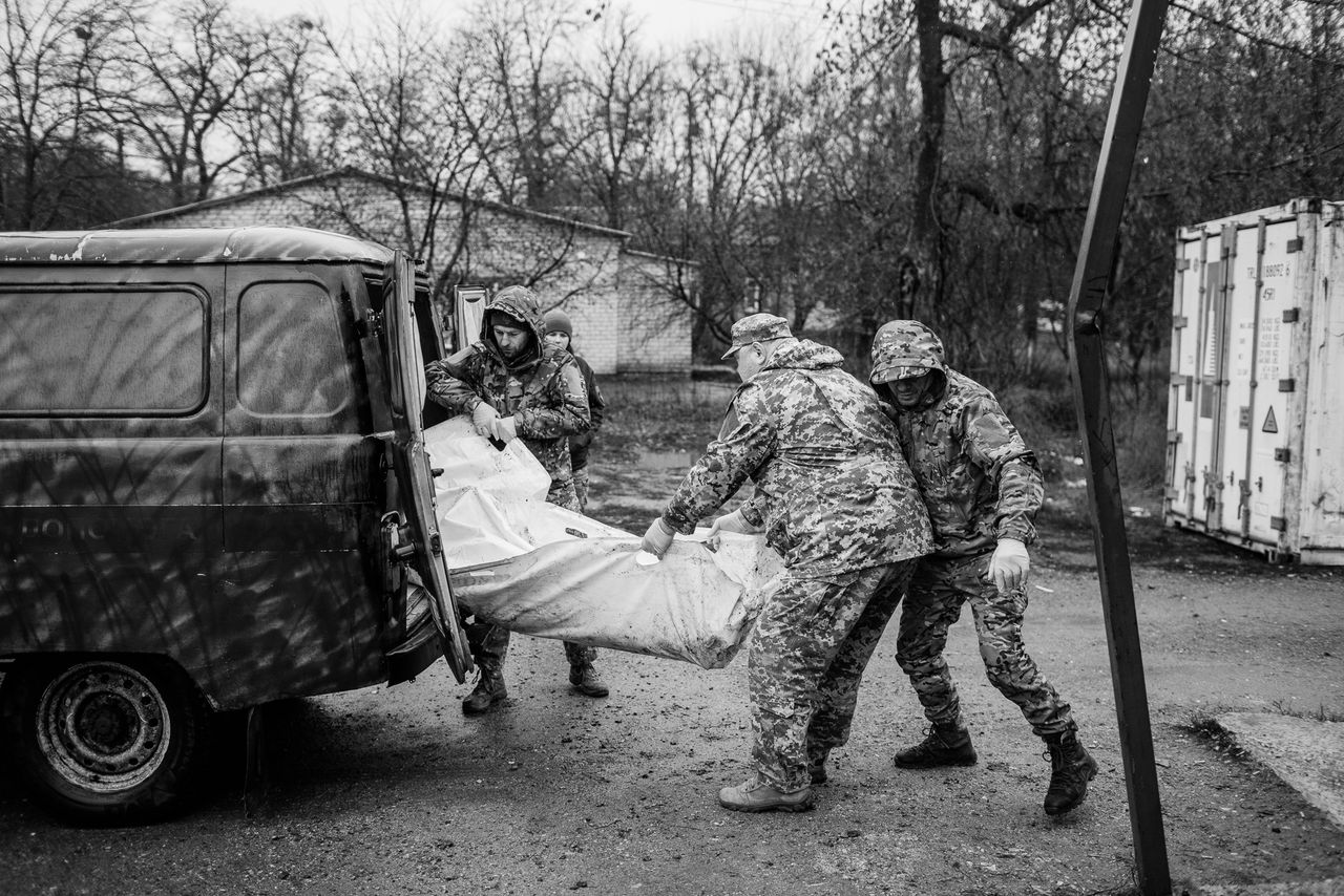 The soldiers are transferring bodies from the transport vehicle to the morgue.