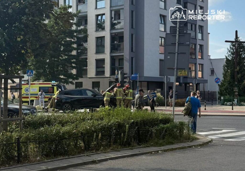Grupa strażaków w mundurach pomaga przy usuwaniu zniszczeń po wypadku drogowym na ruchliwej ulicy.