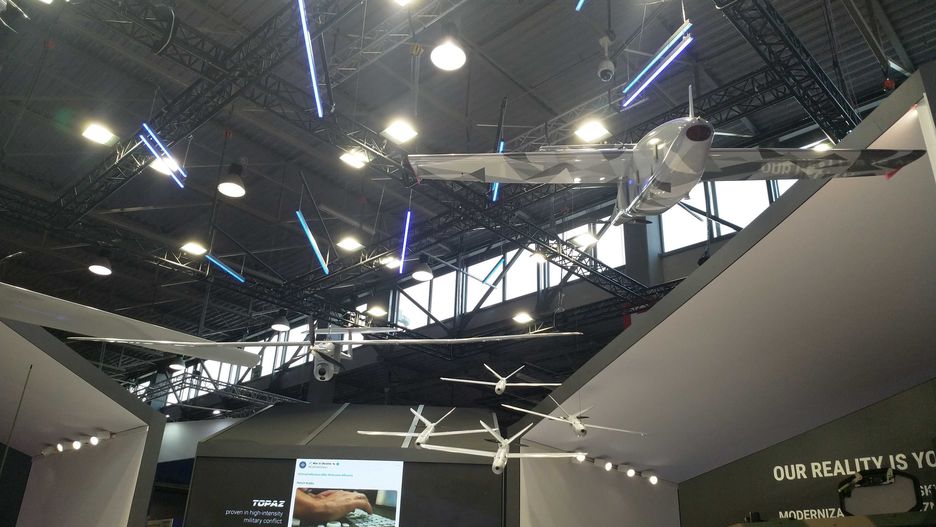 Podwieszony dron FlyEye w otoczeniu mniejszych Warmate i większego FT5 podczas MSPO 2023.
