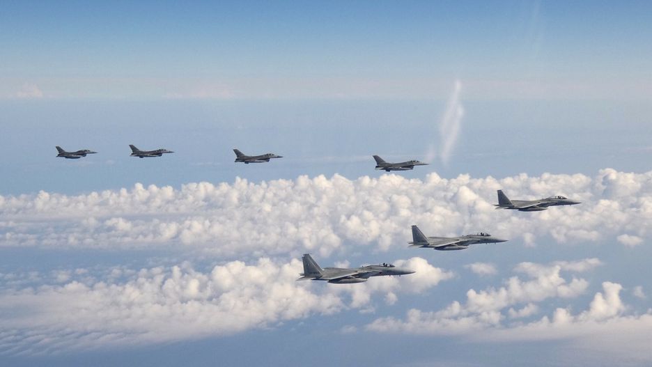 Samoloty bojowe F-15 z przodu i cztery myśliwce F-16 przelatują nad Morzem Japońskim
