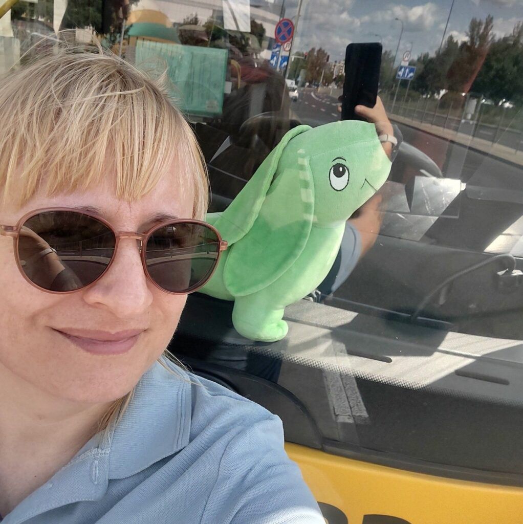 Kobieta w okularach przeciwsłonecznych robi selfie z pluszowym zielonym królikiem na tylnej szybie samochodu.