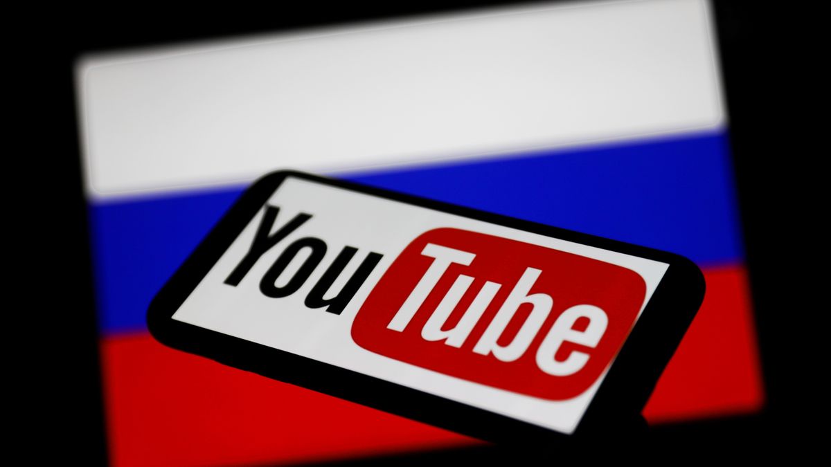 YouTube logo displayed on a phone screen and Russian flag displayed on a screen in the background are seen in this illustration photo taken in Krakow, Poland on March 1, 2022. (Photo Illustration by Jakub Porzycki/NurPhoto via Getty Images)