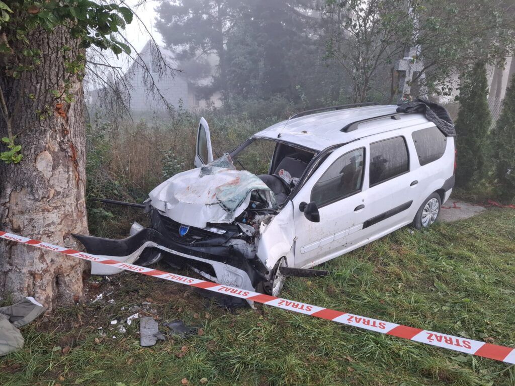 Rozbity samochód osobowy stoi przy drzewie, otoczony taśmą policyjną w mistycznej, porannej mgle.