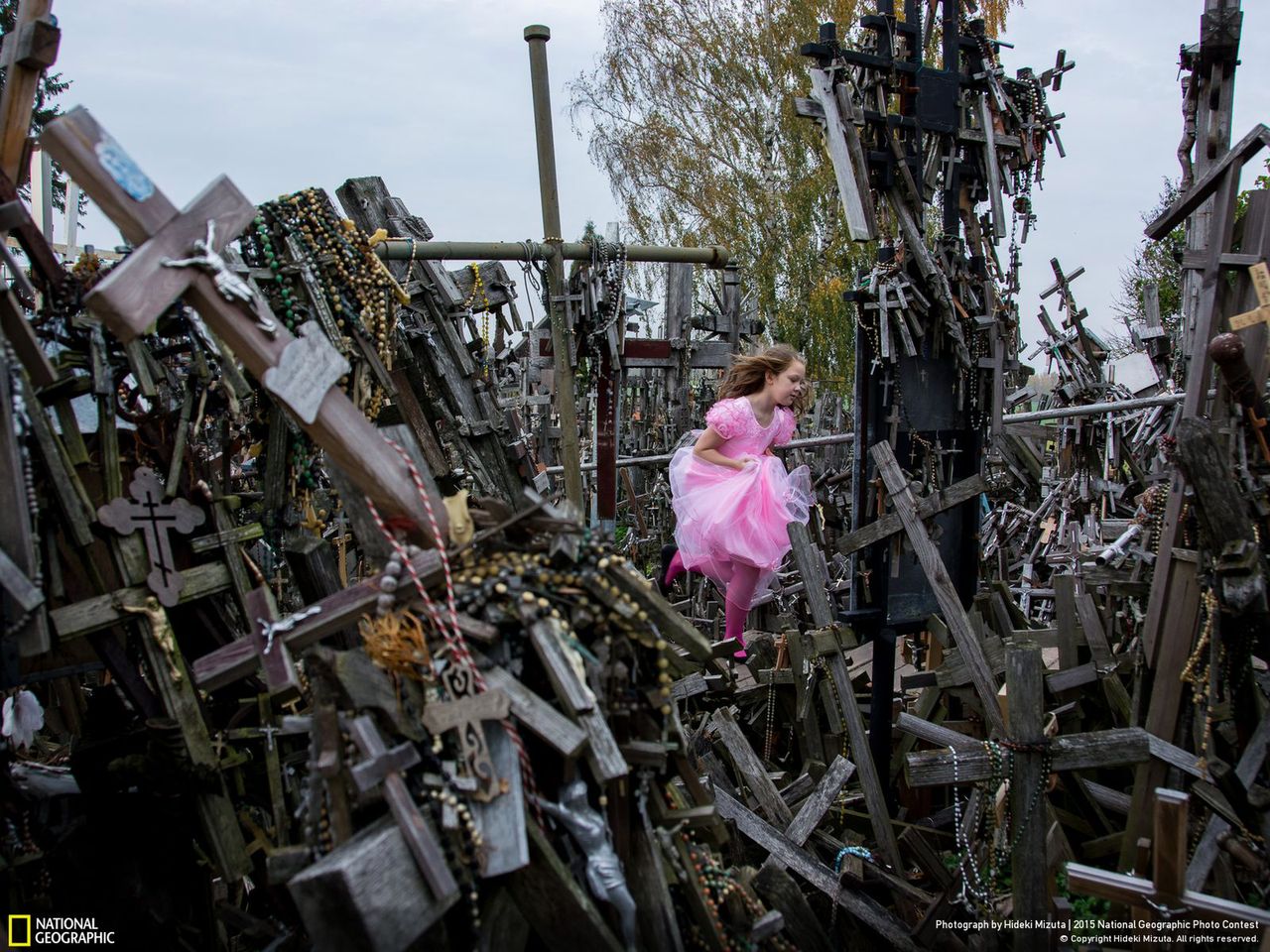Pierwsze z honorowo wyróżnionych zdjęć autorstwa Hideki Mizuta przedstawia dziewczynkę w stroju wróżki biegającą wśród lasu krzyży. „Hill of Crosses” to fotografia opowiadająca o katolickim oporze względem prześladowań na Litwie.