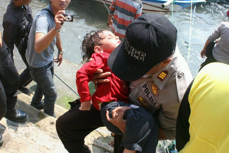 Policjant trzyma dziecko uratowane z łodzi, która zatonęłą <br/>w pobliżu wybrzeży Indonezji