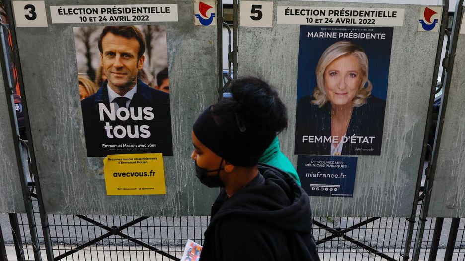 People walk past official campaign posters of French presidential election candidates Marine le Pen, leader of French far-right National Rally (Rassemblement National) party, and French President Emmanuel Macron, candidate for his re-election, displayed on bulletin boards in Paris, France, April 4, 2022.