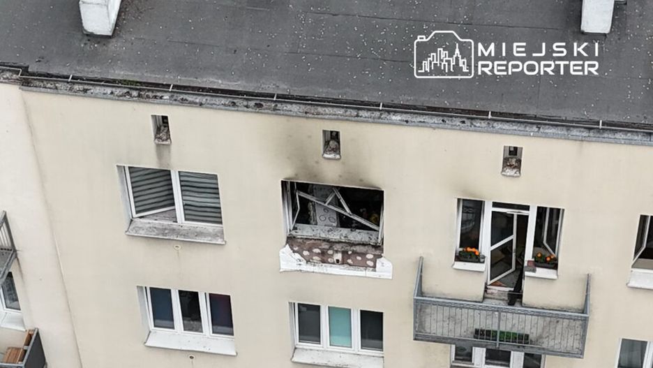 Uszkodzone okno na trzecim piętrze budynku mieszkalnego z widocznymi resztkami materiałów budowlanych.