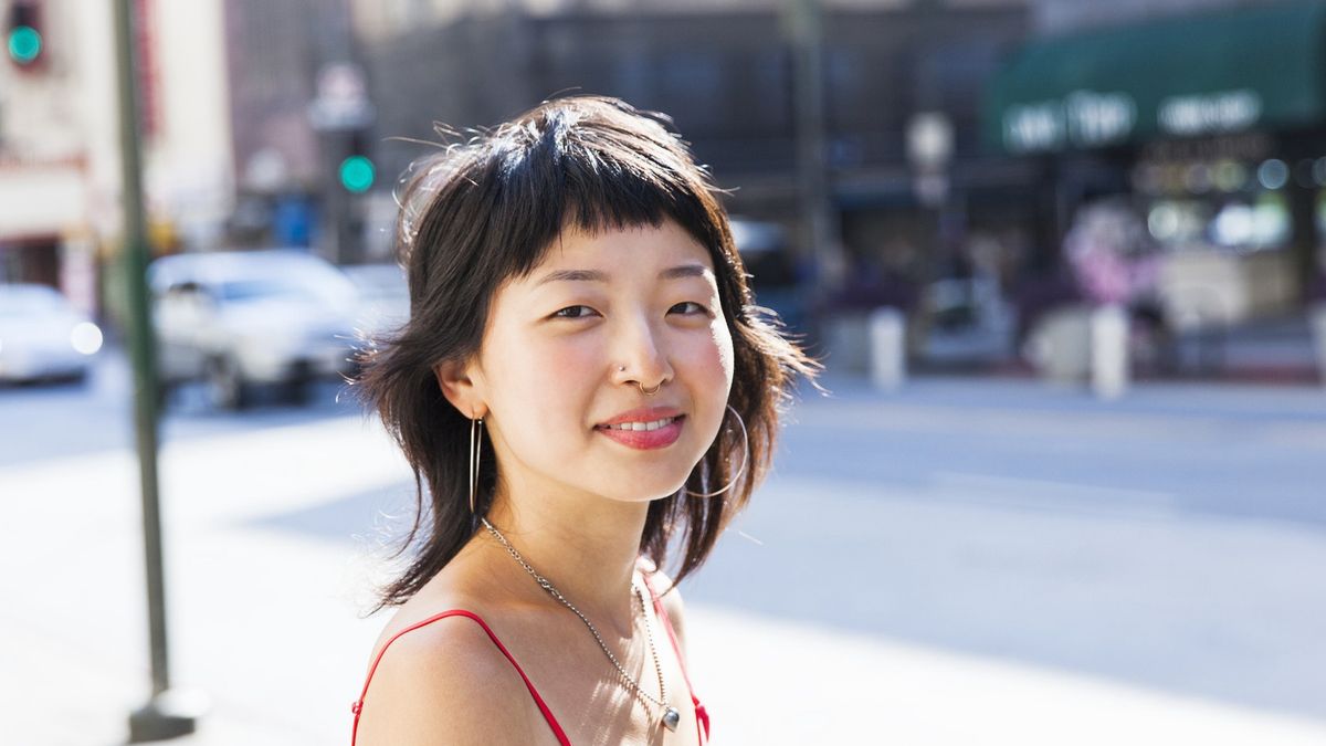 Young woman looking at camera smiling
Young Asian woman with a rose ring looking at the camera smiling with a city street scene out of focus in the background
Stephen Zeigler