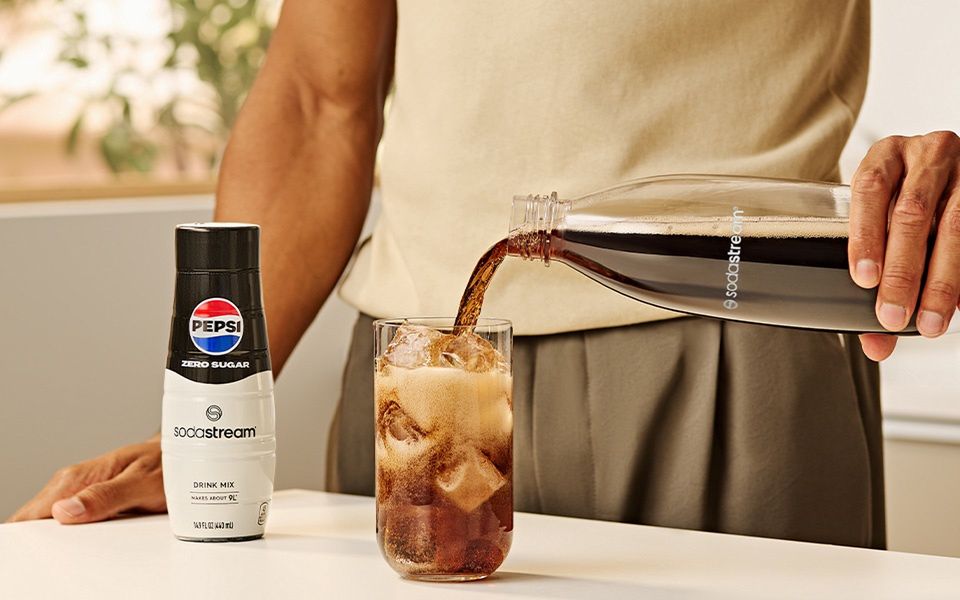 Mężczyzna nalewający do szklanki Pepsi zrobioną w saturatorze SodaStream - zdjęcie. 